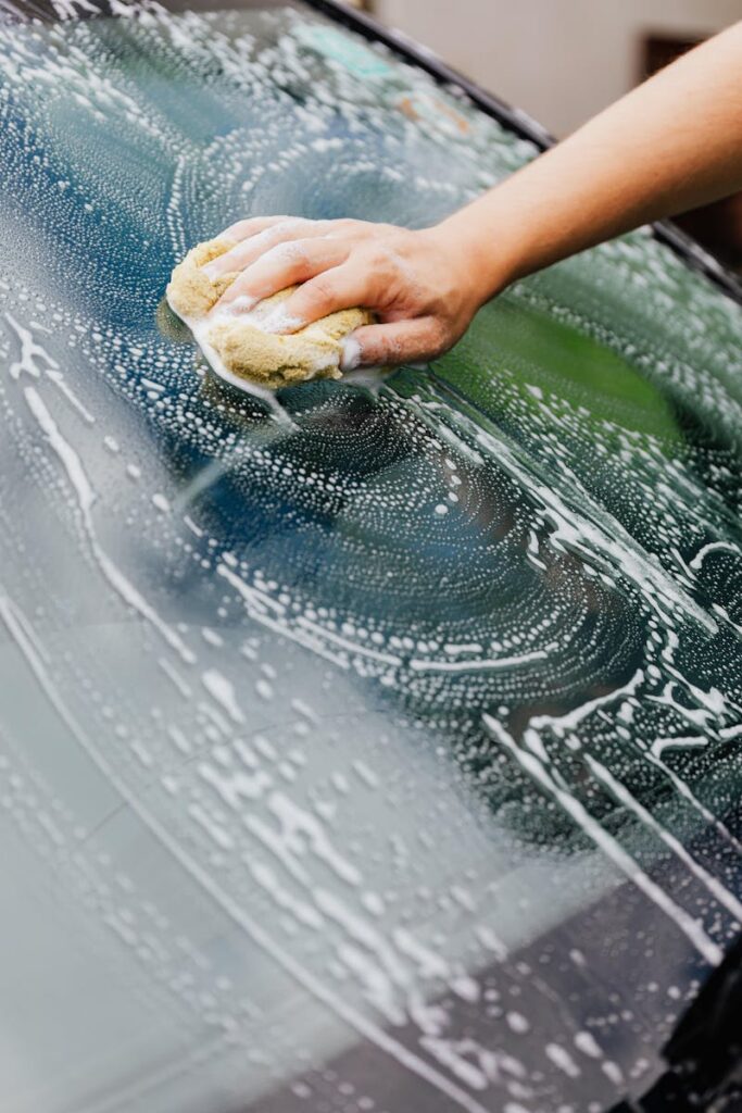 Close-up of a hand washing a car windshield with a soapy sponge, detailing care.