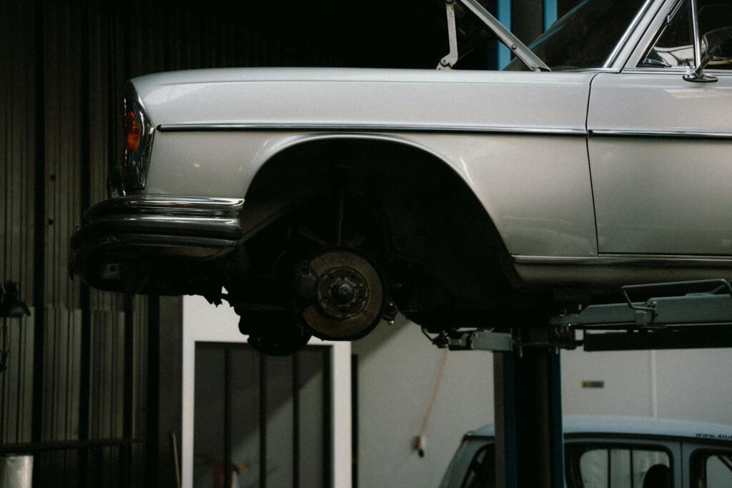 A classic car is elevated on a lift in a professional auto repair garage, showcasing its undercarriage.