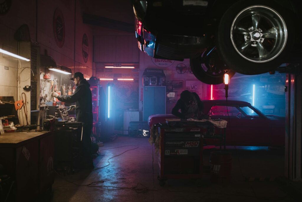 Mechanics working in a neon-lit garage, focusing on tools and car repairs under vibrant lights.