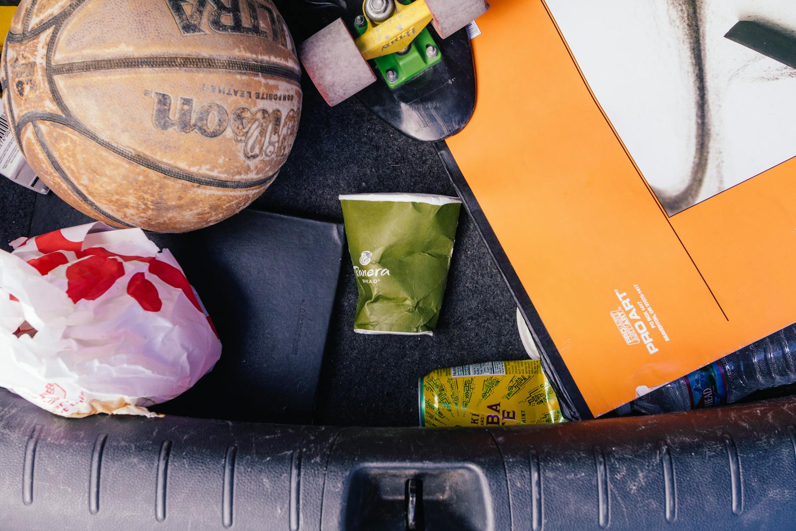 Close-up of basketball, papers, and trash in a car trunk, illustrating untidiness. car trash can