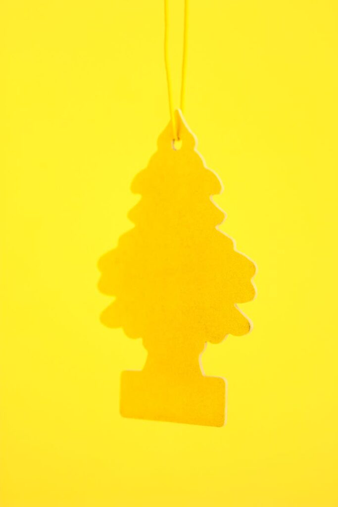 Close-up of a yellow tree-shaped car air freshener hanging against a bright yellow background.