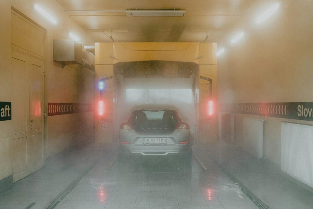 A vehicle inside an automated car wash, surrounded by mist and interior lighting.