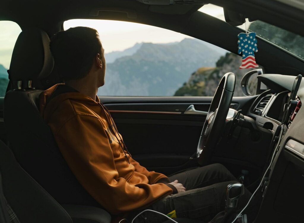 A man in a car admires the scenic mountain view through the window, wearing a casual hoodie.