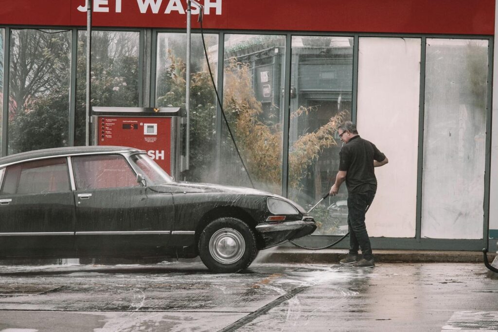 A man cleaning a classic car using a jet wash at an outdoor car wash in Dublin, Ireland.