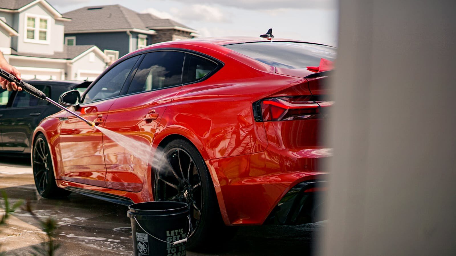 A vibrant red luxury car being washed outdoors in a suburban residential area.