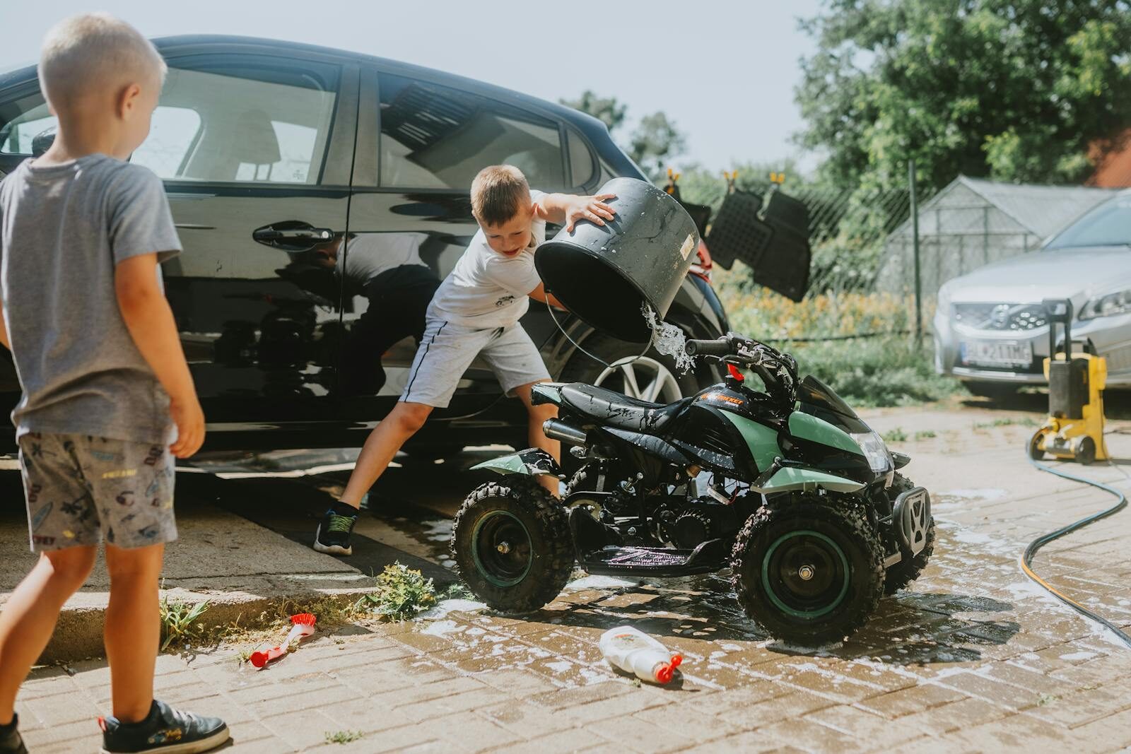 Kids washing a toy car with soap and water on a sunny day, playful summer activity.