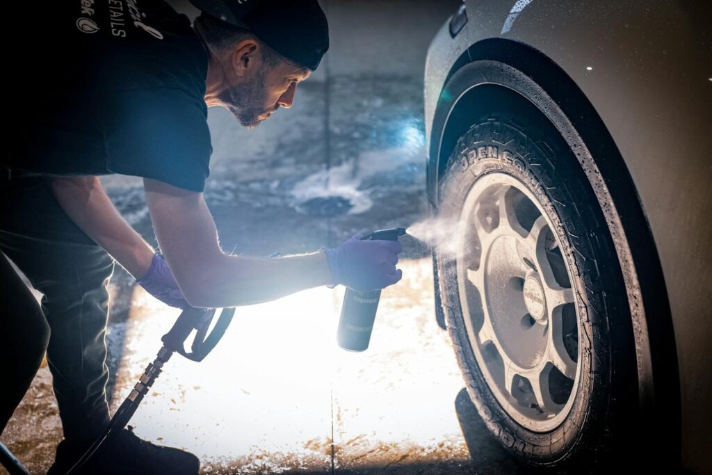 A man meticulously cleaning a car tire with a spray bottle in a vehicle detailing shop.