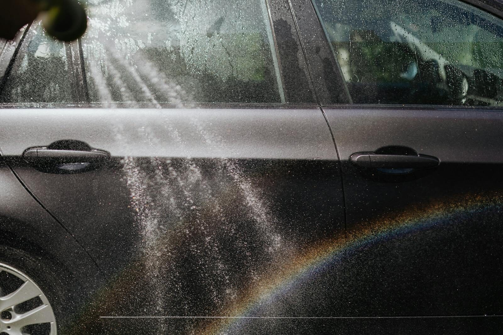 Photo by www.kaboompics.com Close-up of a car being washed with a visible rainbow in sunlight.