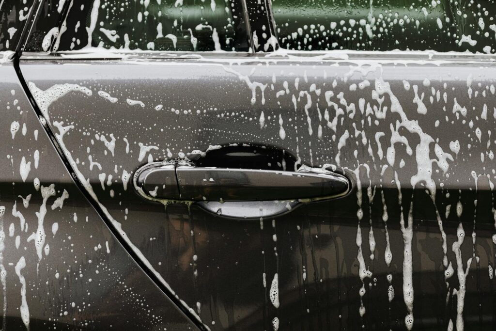 Detailed close-up of soap suds on a black car door during a wash, highlighting automotive care.