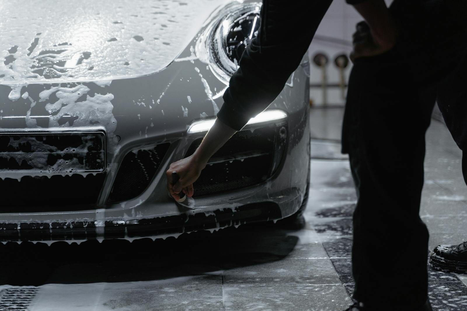 A close-up view of a car being meticulously washed with soap in a garage setting, emphasizing cleanliness and care.
