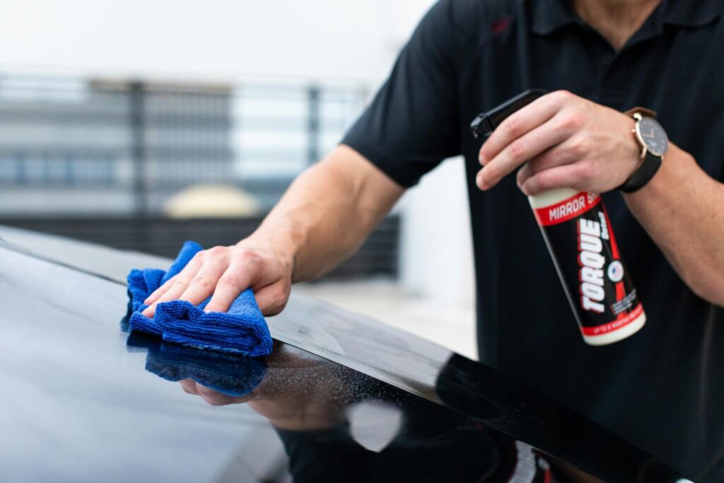Hands cleaning car with microfiber cloth and spray cleaner for a shiny finish.