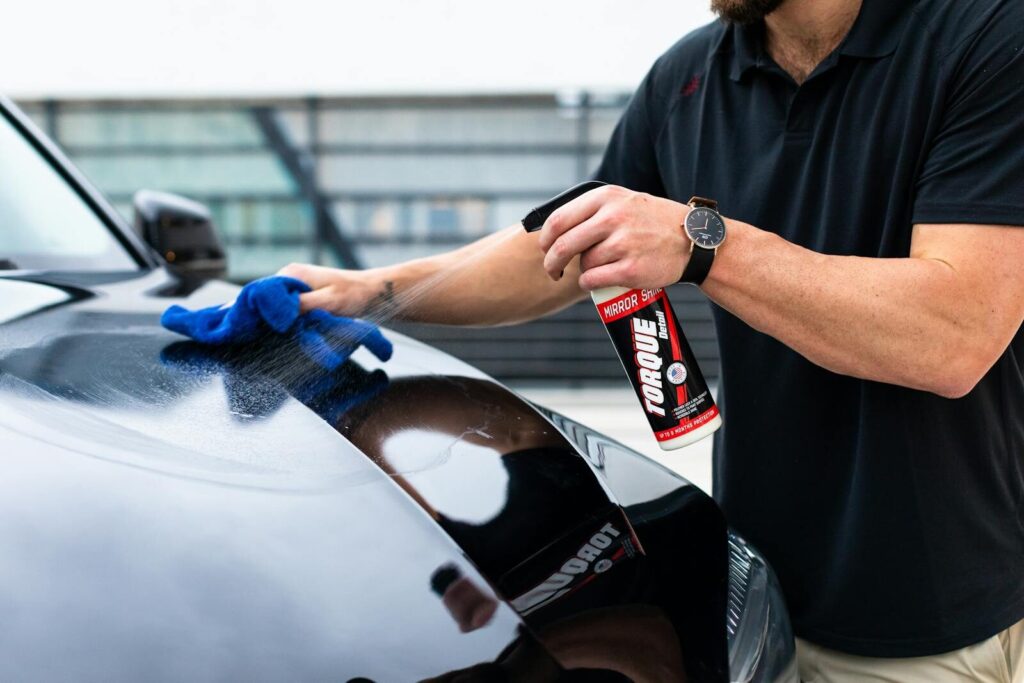 A man cleaning a black car hood with a spray and microfiber cloth.