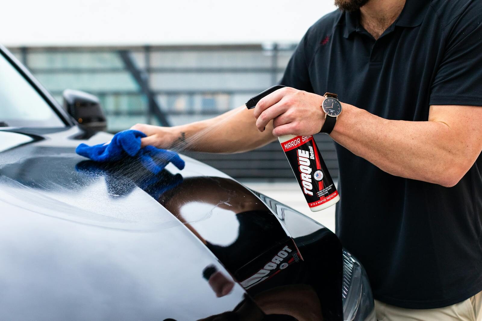 Photo by Torque Detail A man cleaning a black car hood with a spray and microfiber cloth.