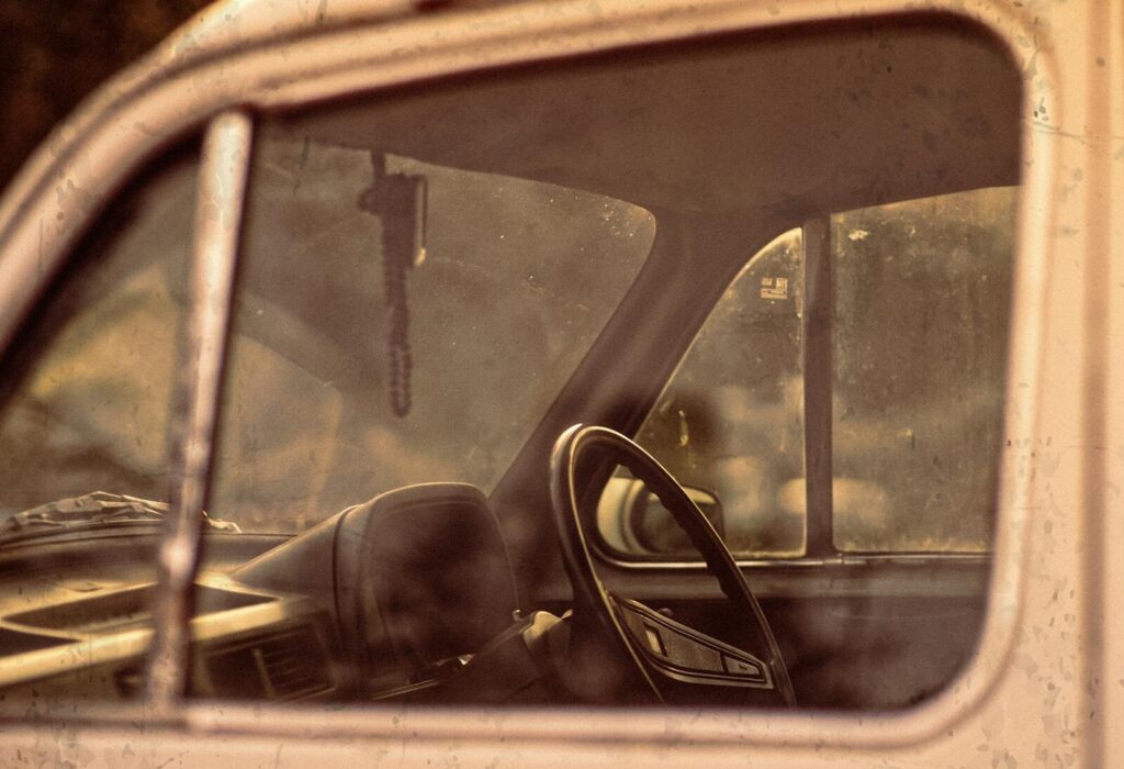 Close-up view of a vintage vehicle's interior showing the steering wheel through the side window. Warm tones.