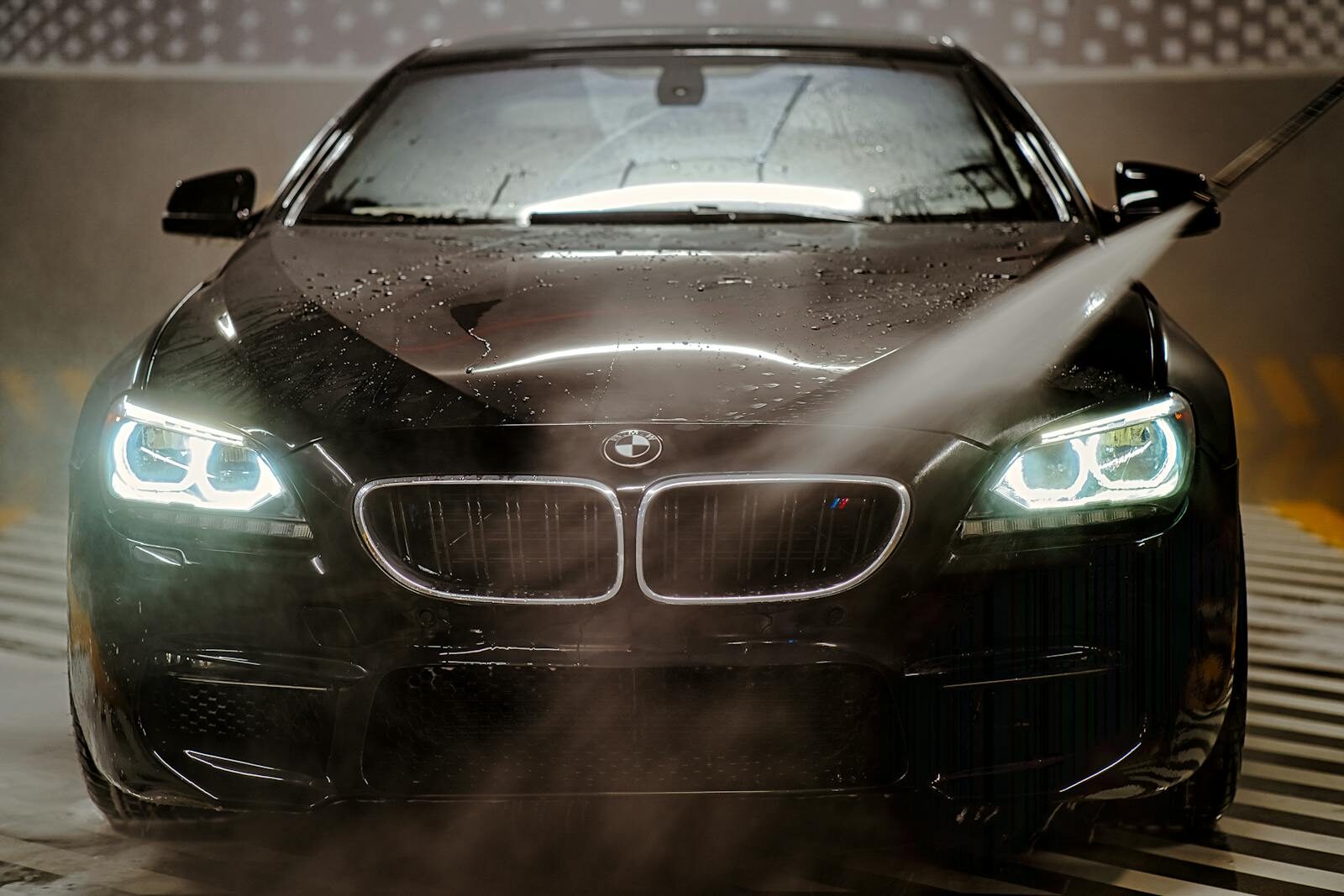 A sleek BMW being washed with water spray at night, highlighting the headlights and wet reflections.