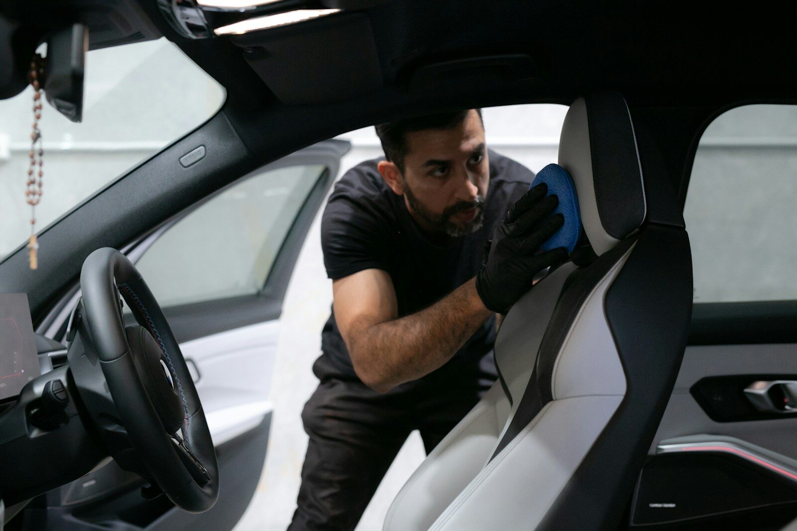 Photo by Fine Automotive Detailing A man cleans a car seat inside the vehicle.
