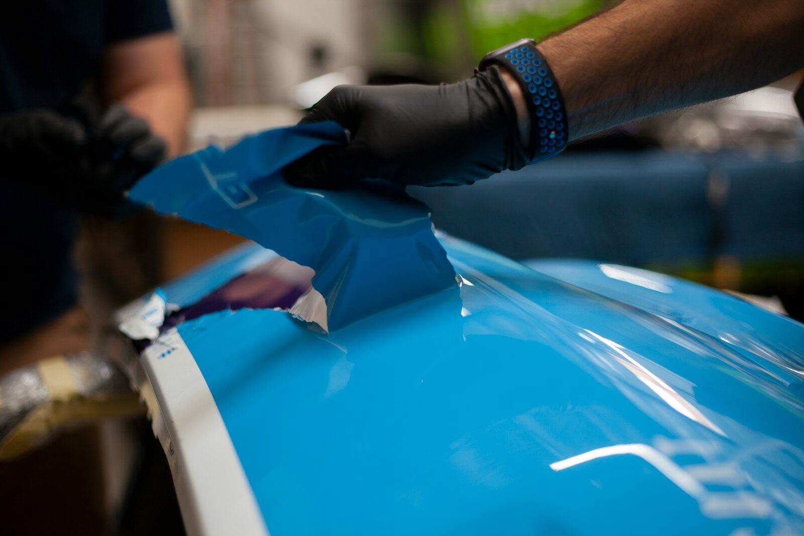 Photo by Clarity Coat a person wearing gloves and gloves is painting a blue car