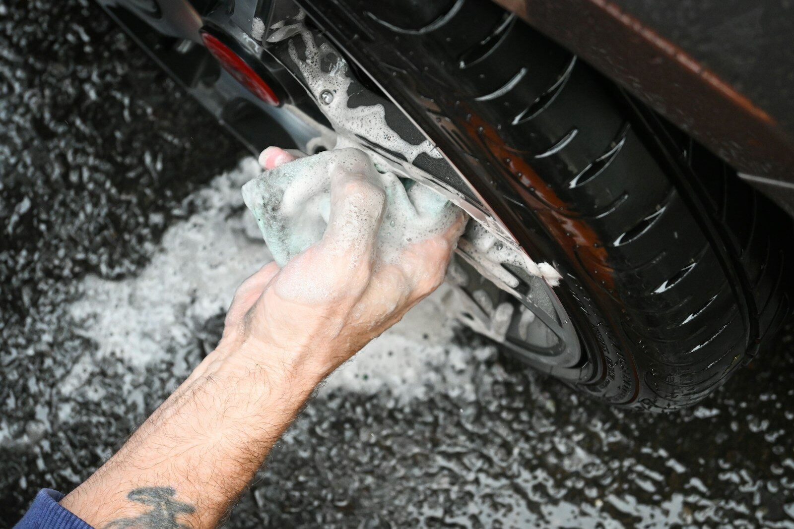 Photo by Nik a man washing a car tire with a rag