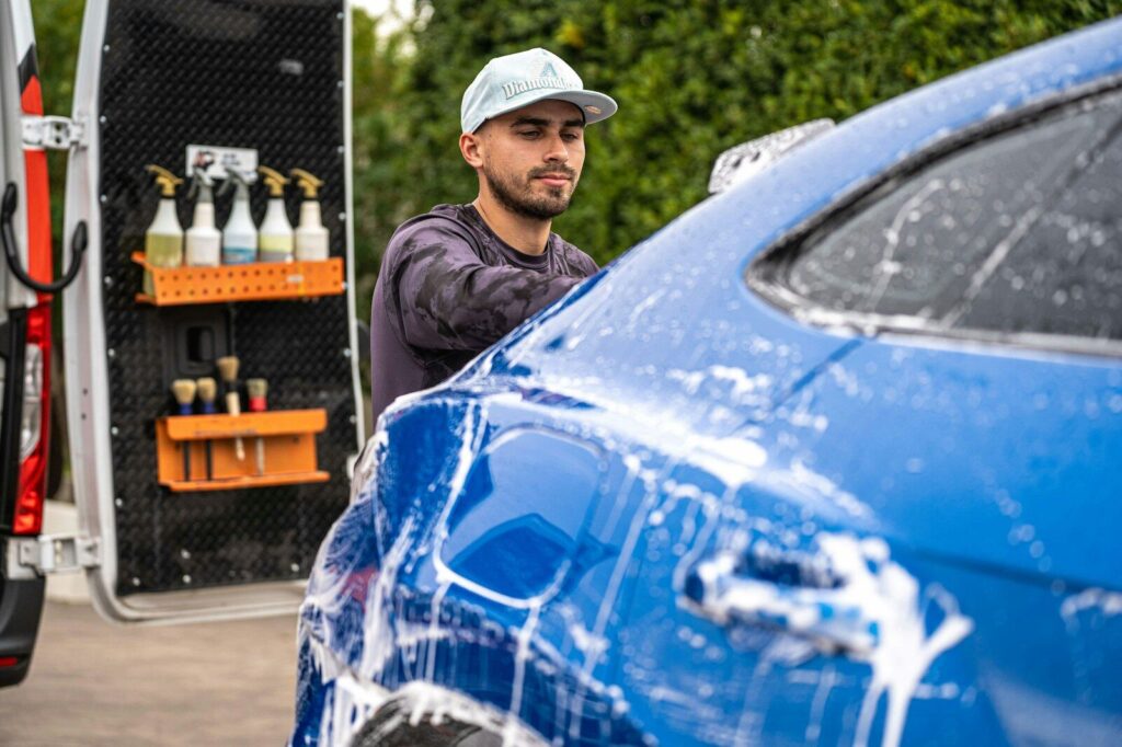 A man washes a blue car with soap.