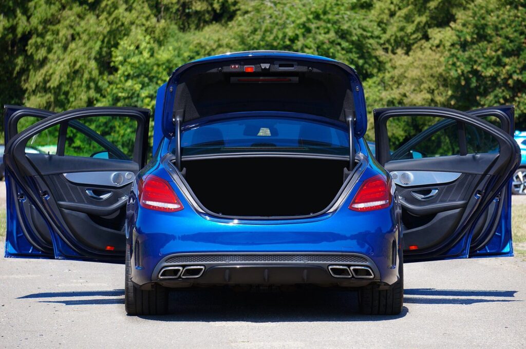 Blue luxury sedan with open doors and trunk parked in a lot.