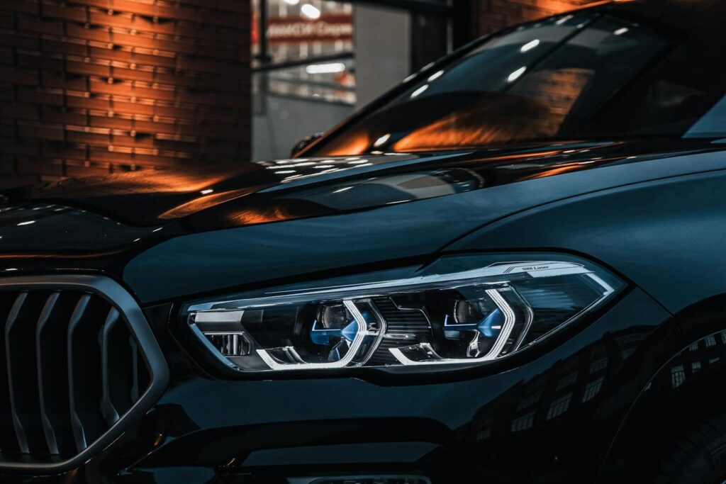 Close-up of a shiny black car with illuminated headlights and sleek design in an urban setting.